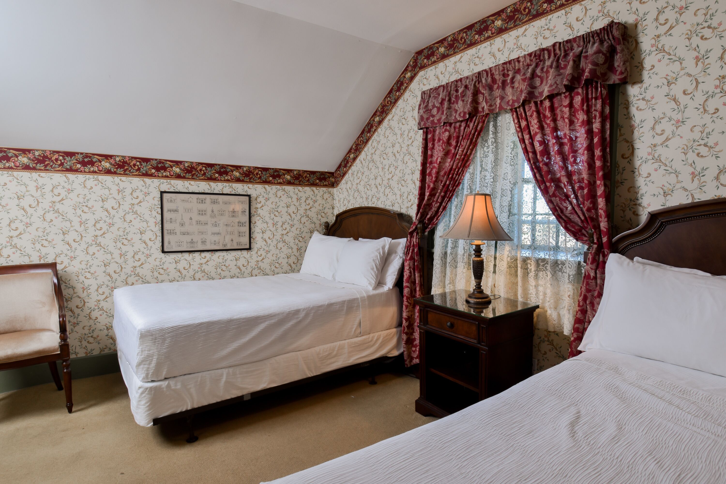 Une chambre avec deux lits, une table de chevet en bois, une chaise et une fenêtre avec des rideaux.