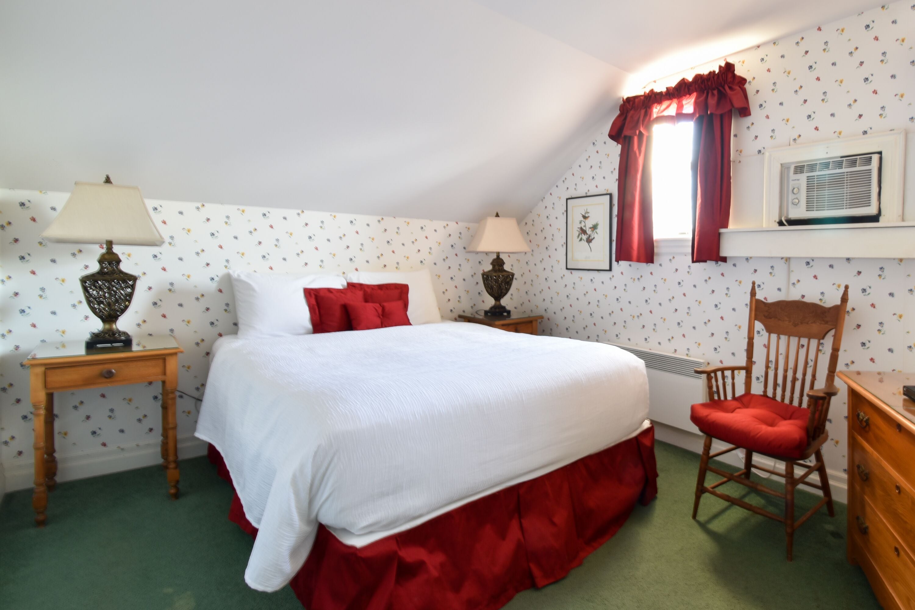 A bedroom with a bed, two bedside tables, a chair, a dresser, a window with curtains, and a wall-mounted air conditioner.