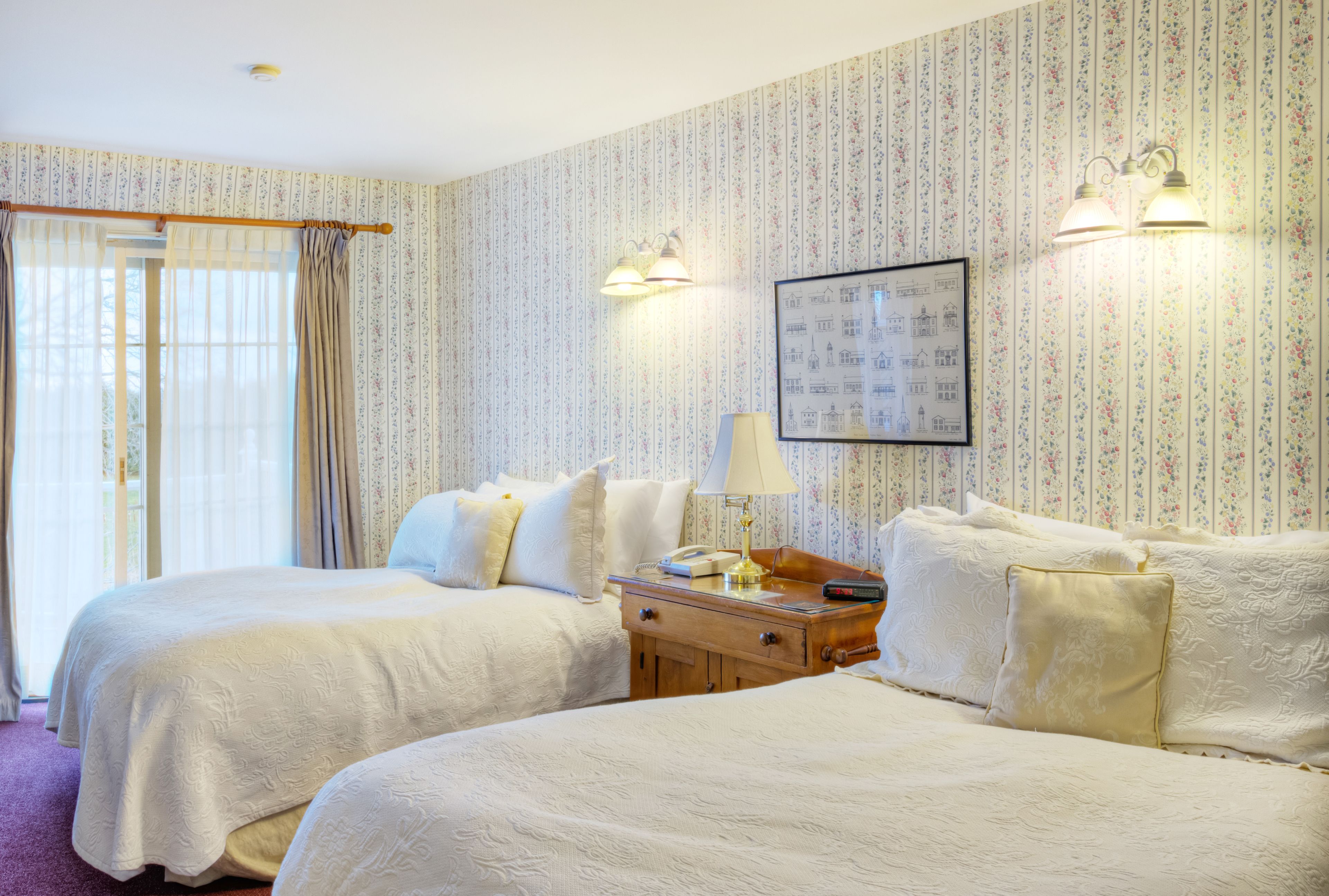 A hotel room with two beds, a nightstand, a lamp, and a framed picture on the wall.