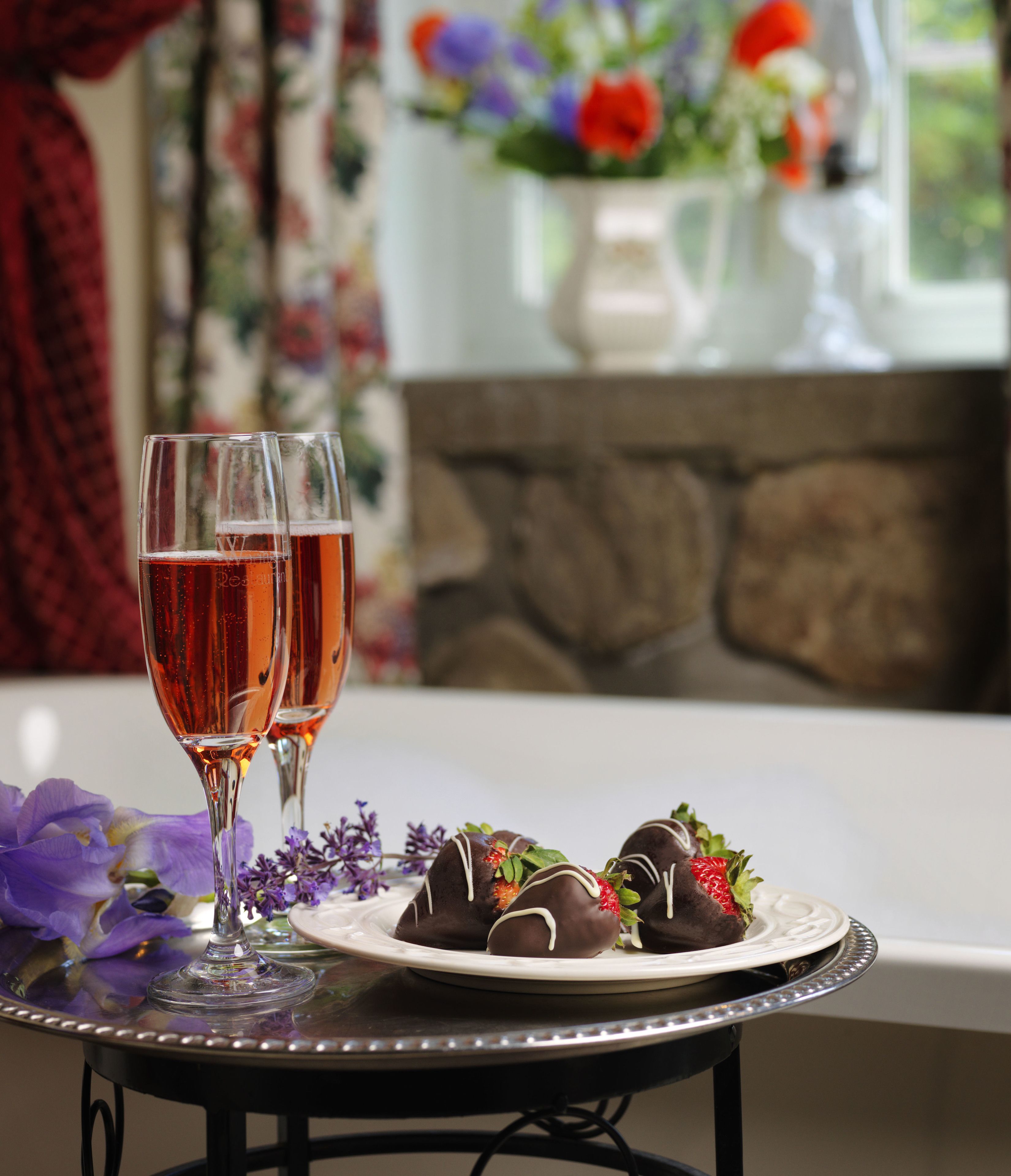 A table with two glasses of red wine and chocolate-covered strawberries on a plate.