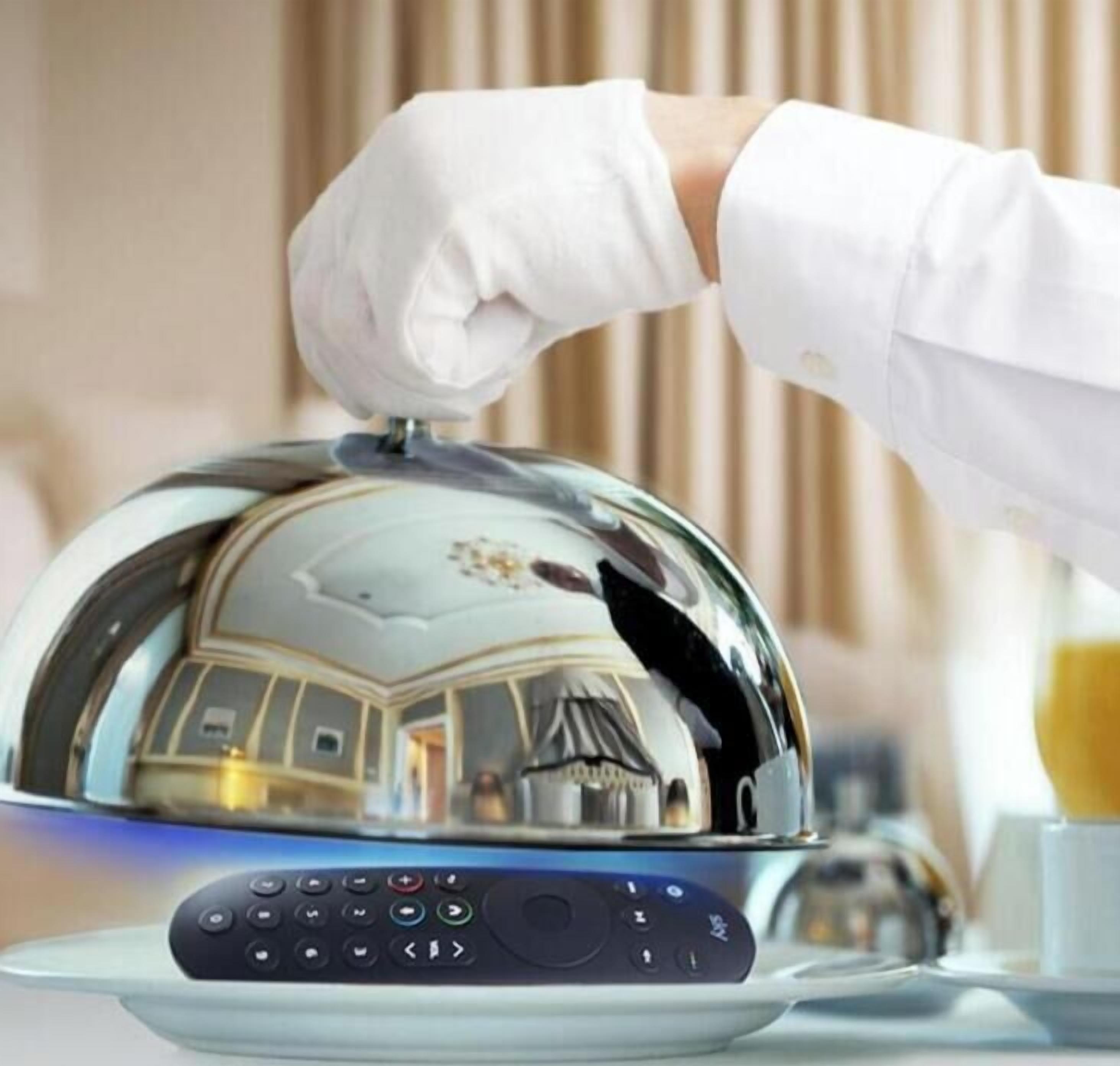 A person in a white glove lifting a reflective, domed service item, likely a food warmer, with a control panel below it.