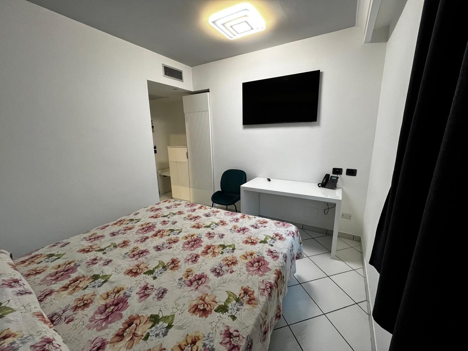 Een slaapkamer met een bed, een bureau, een stoel, een televisie en een telefoon.