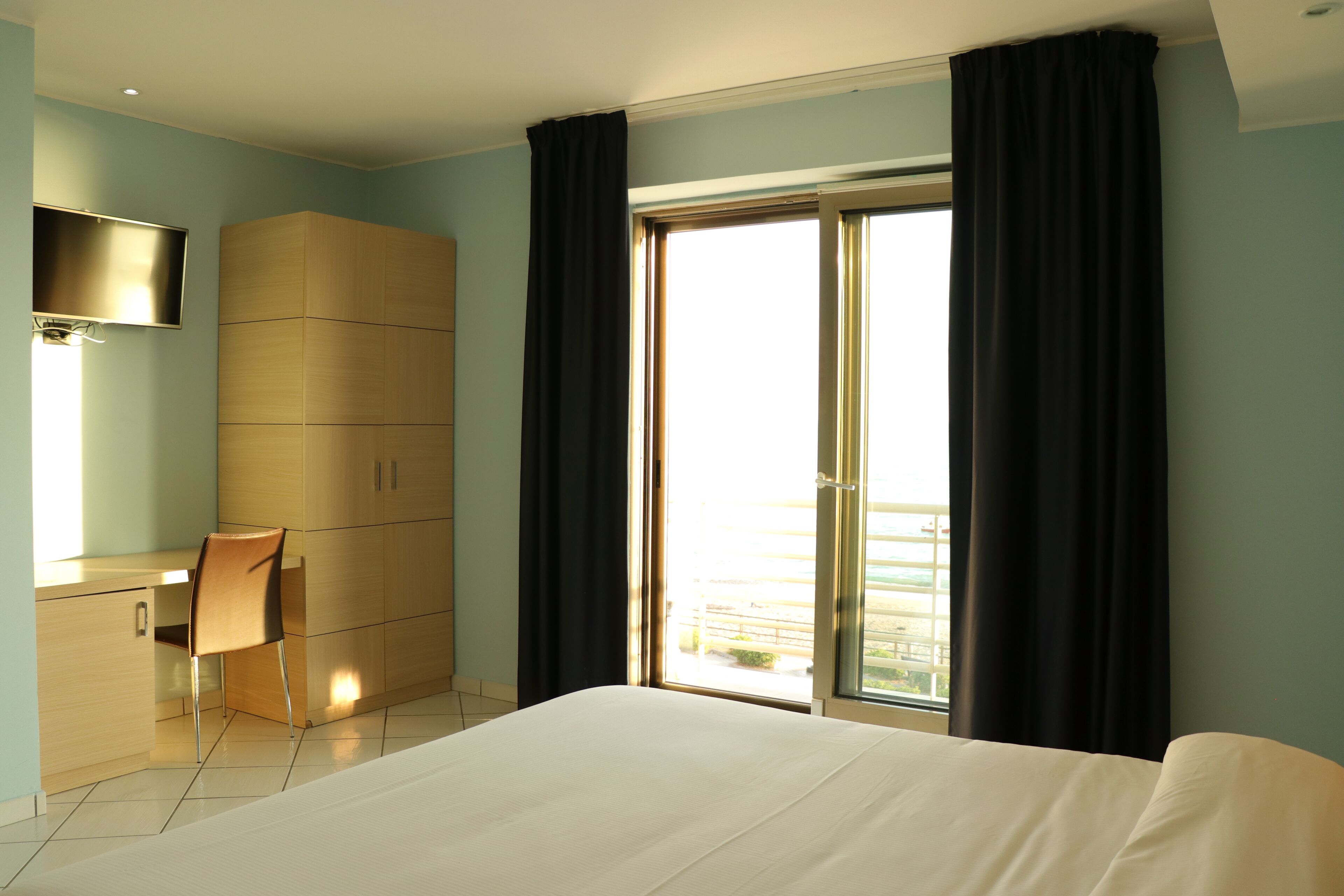 Una habitación de hotel con cama, escritorio, silla, televisor y una ventana grande con cortinas.