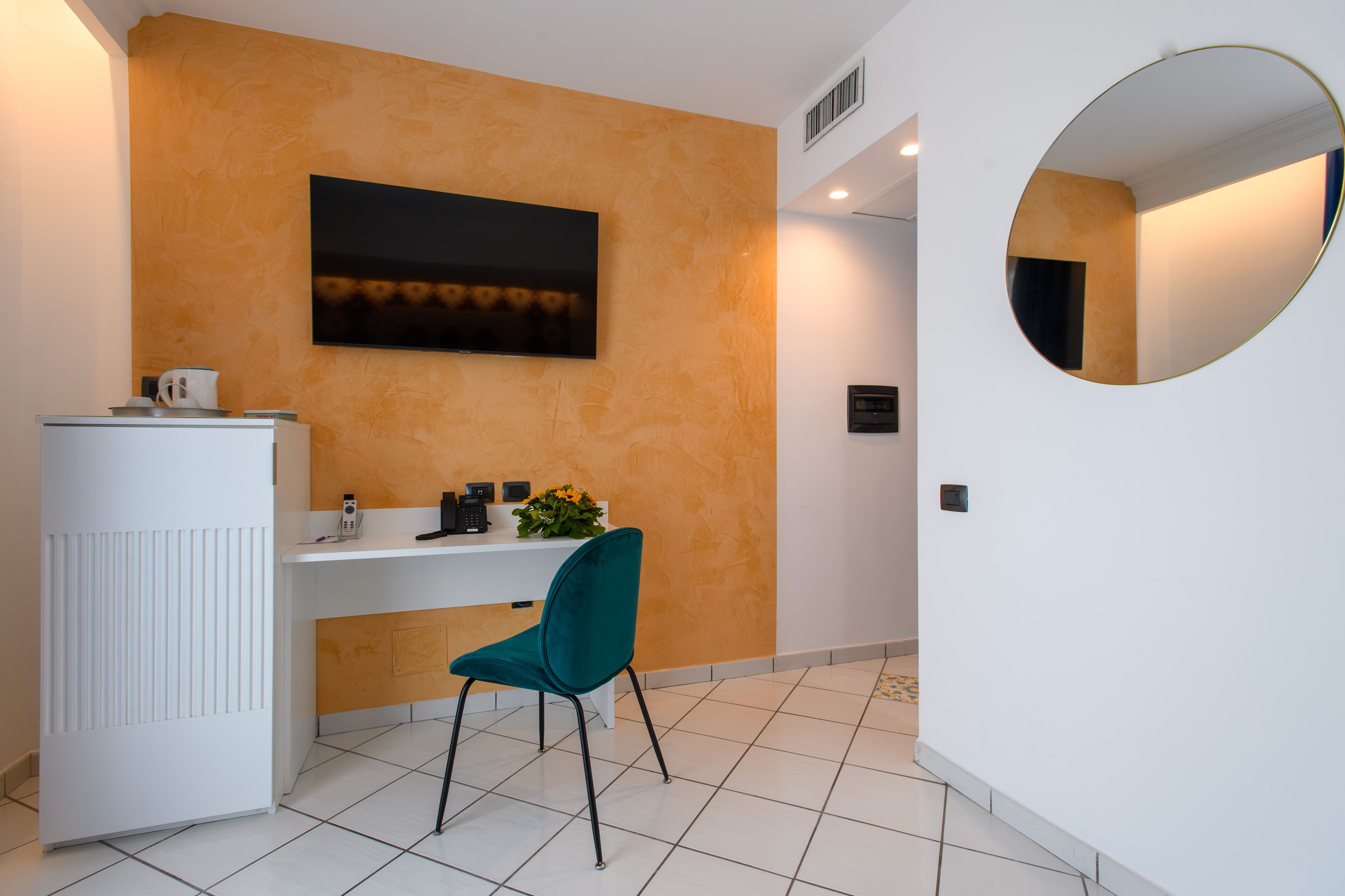 A reception area with a white desk, teal chair, and a large mirror.