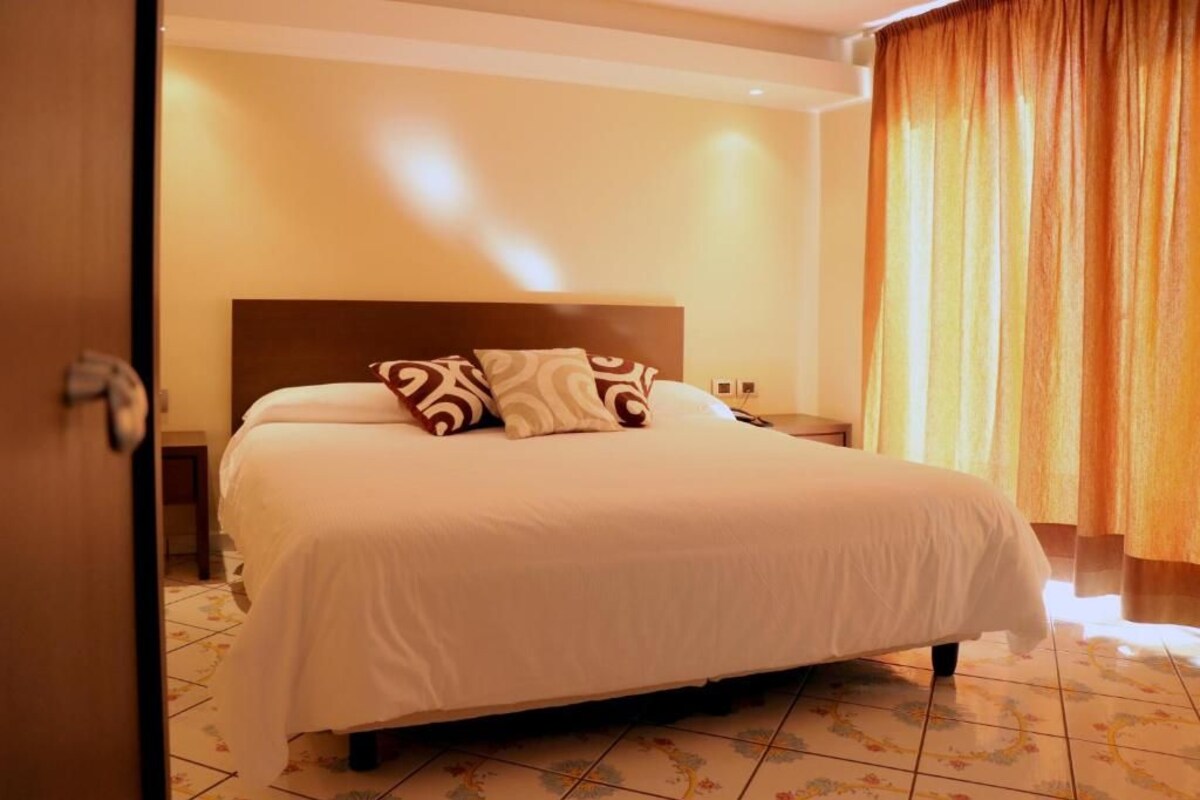 A neatly made bed with a headboard, a nightstand, and a window with curtains.