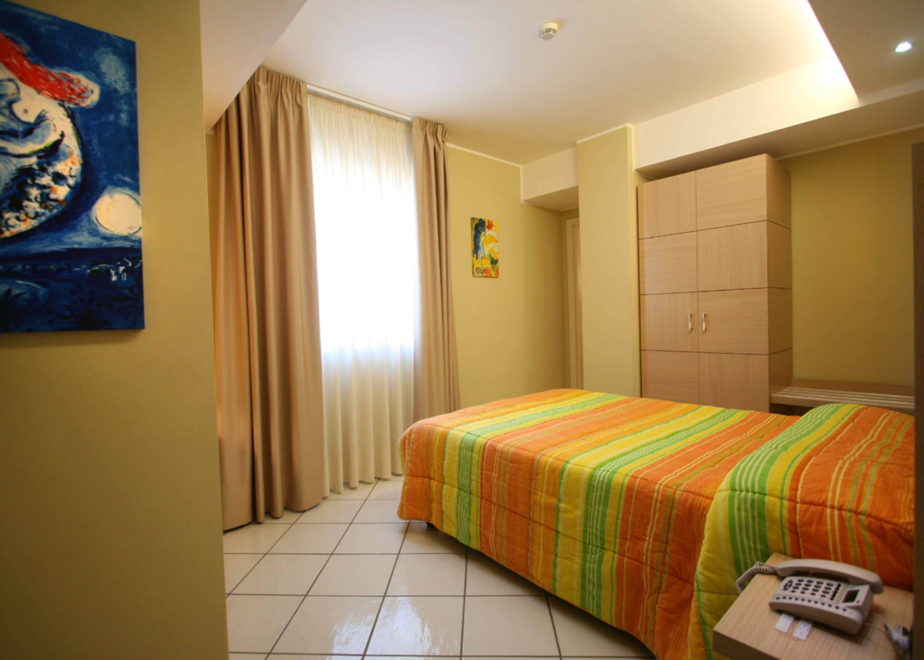 Ein Hotelzimmer mit Bett, Telefon, Schrank und einem Bild an der Wand.