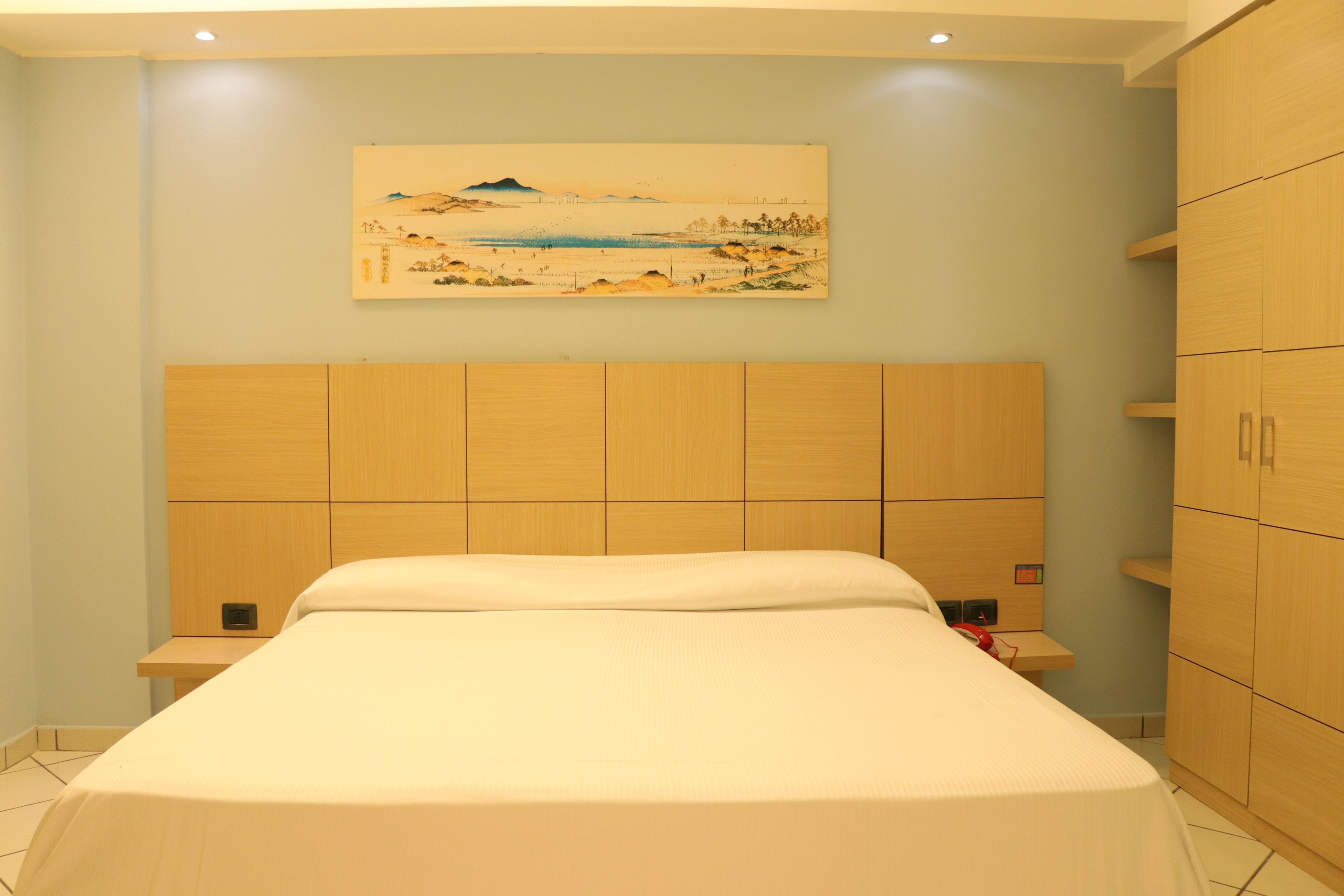 A bedroom with a large bed, wooden headboard, a painting on the wall, and built-in wooden cabinets.