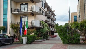 A multi-story residential building with balconies, a paved walkway, and a flagpole with flags. - Rama Palace Hotel (Casalnuovo di Napoli)