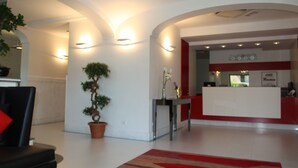 A modern reception area with a reception desk, potted plants, and a red carpet. - Rama Palace Hotel (Casalnuovo di Napoli)