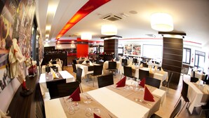 A restaurant with multiple tables set for dining, a bar area, and a red accent wall. - Rama Palace Hotel (Casalnuovo di Napoli)