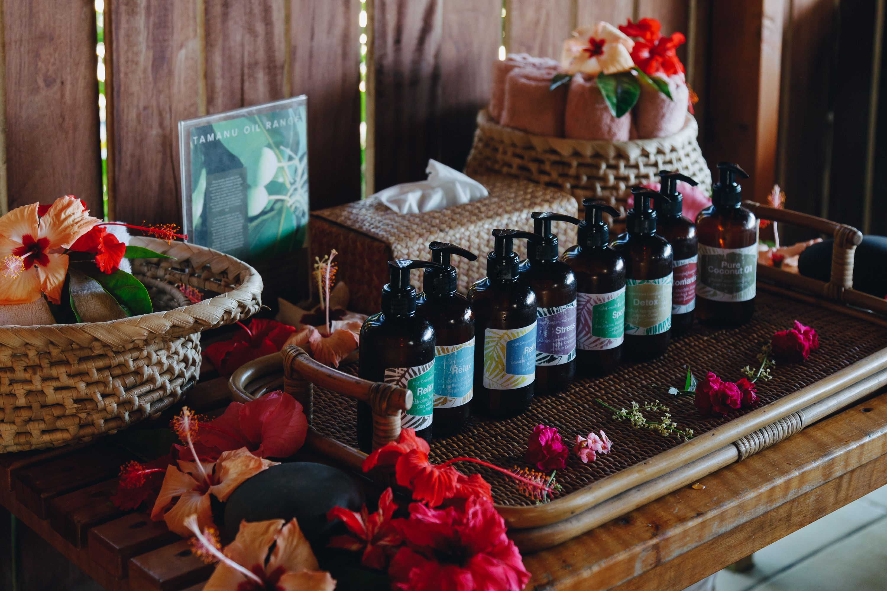 A wooden table with bottles of essential oils, a woven basket with flowers, and a framed picture.