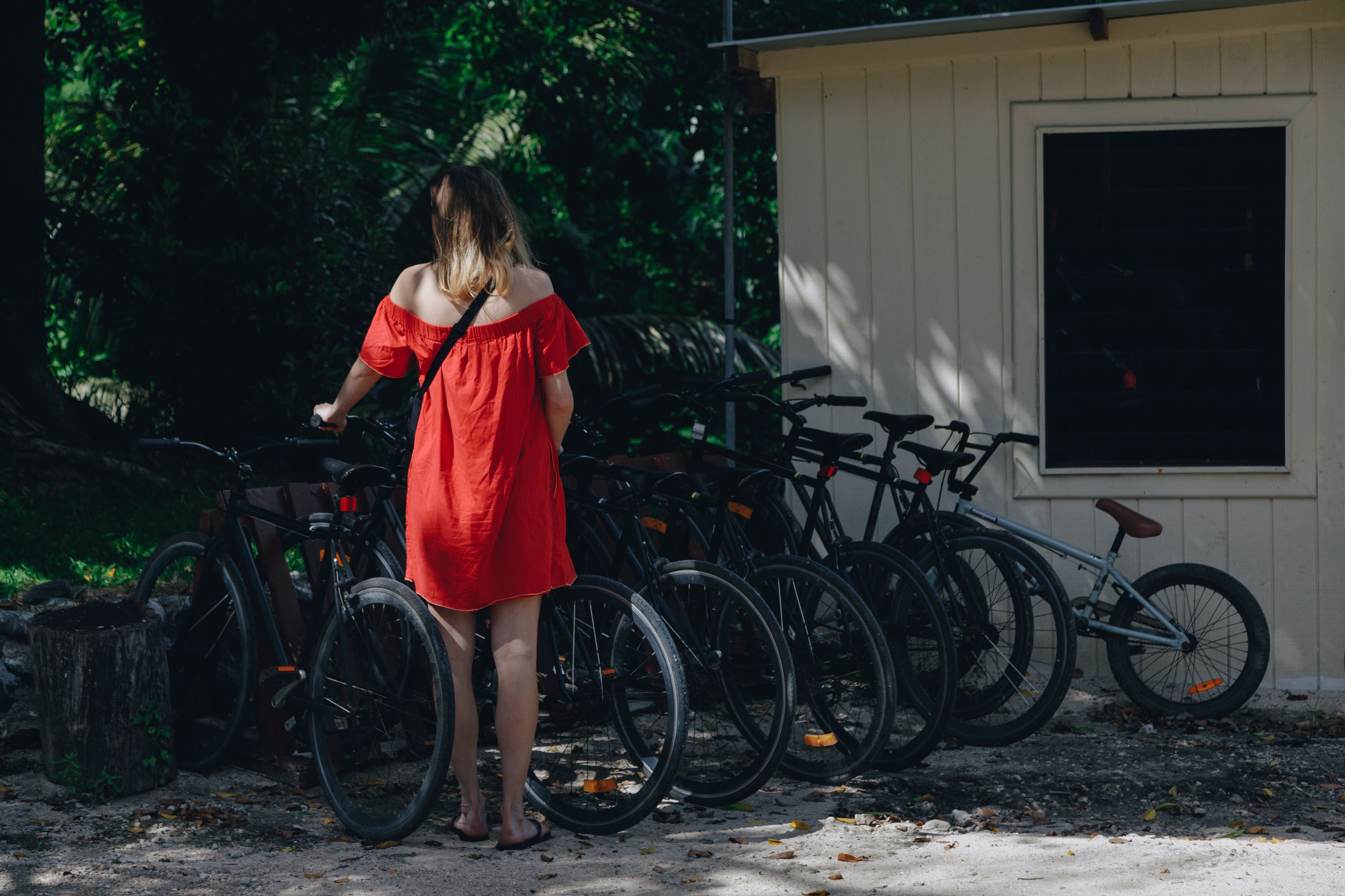 A person in a red dress standing near bicycles parked outside a building with a window.