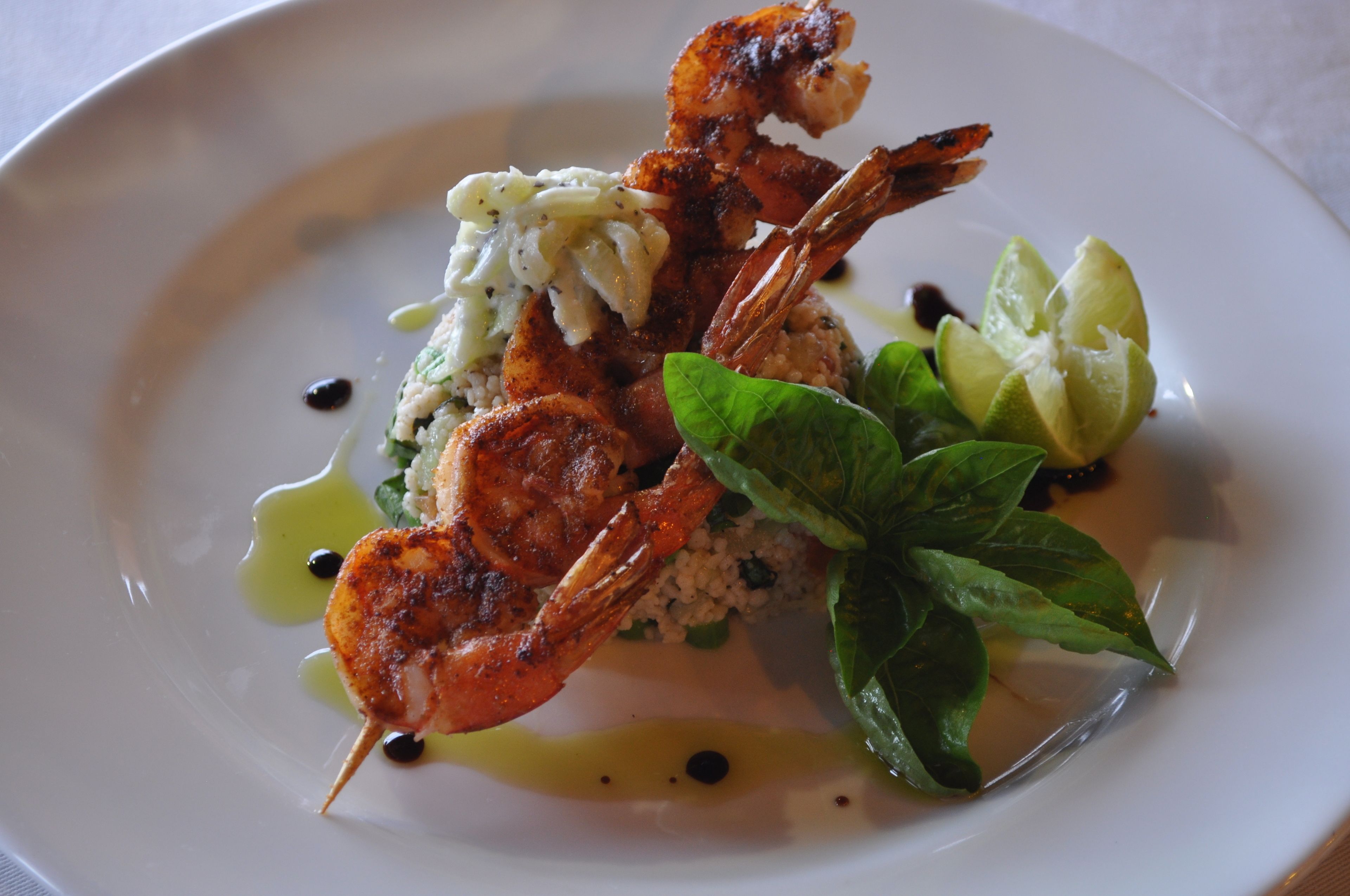 A plate with grilled shrimp, a dollop of sauce, and a basil leaf.