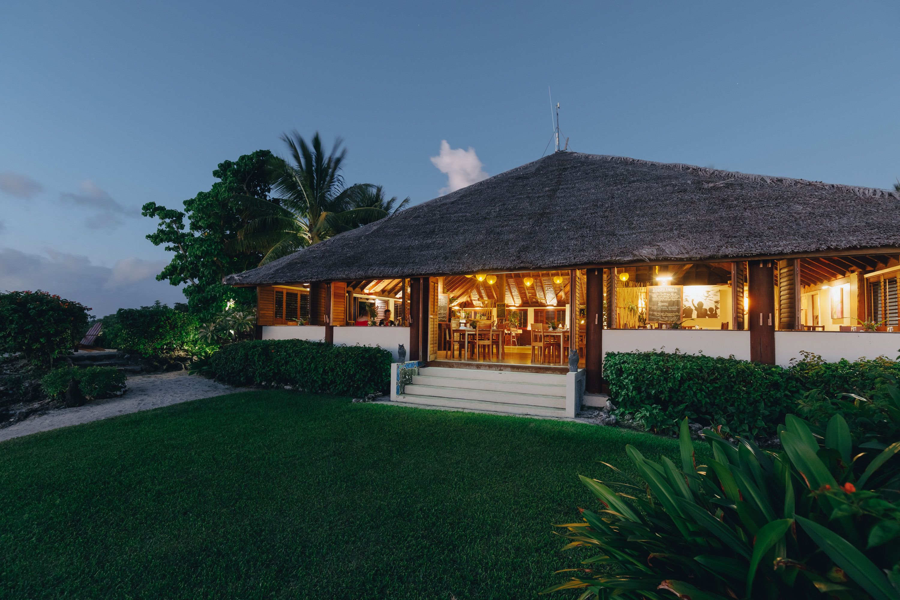 A thatched-roof building with a well-maintained lawn and tropical vegetation.