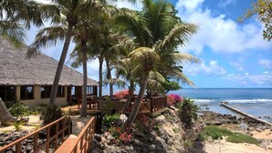 A beachfront property with a thatched-roof building, wooden deck, and palm trees. - White Grass Ocean Resort (Tanna Island)