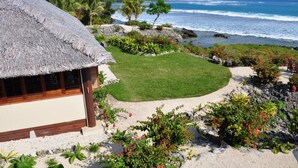 A thatched-roof building with a lawn and tropical plants. - White Grass Ocean Resort (Tanna Island)