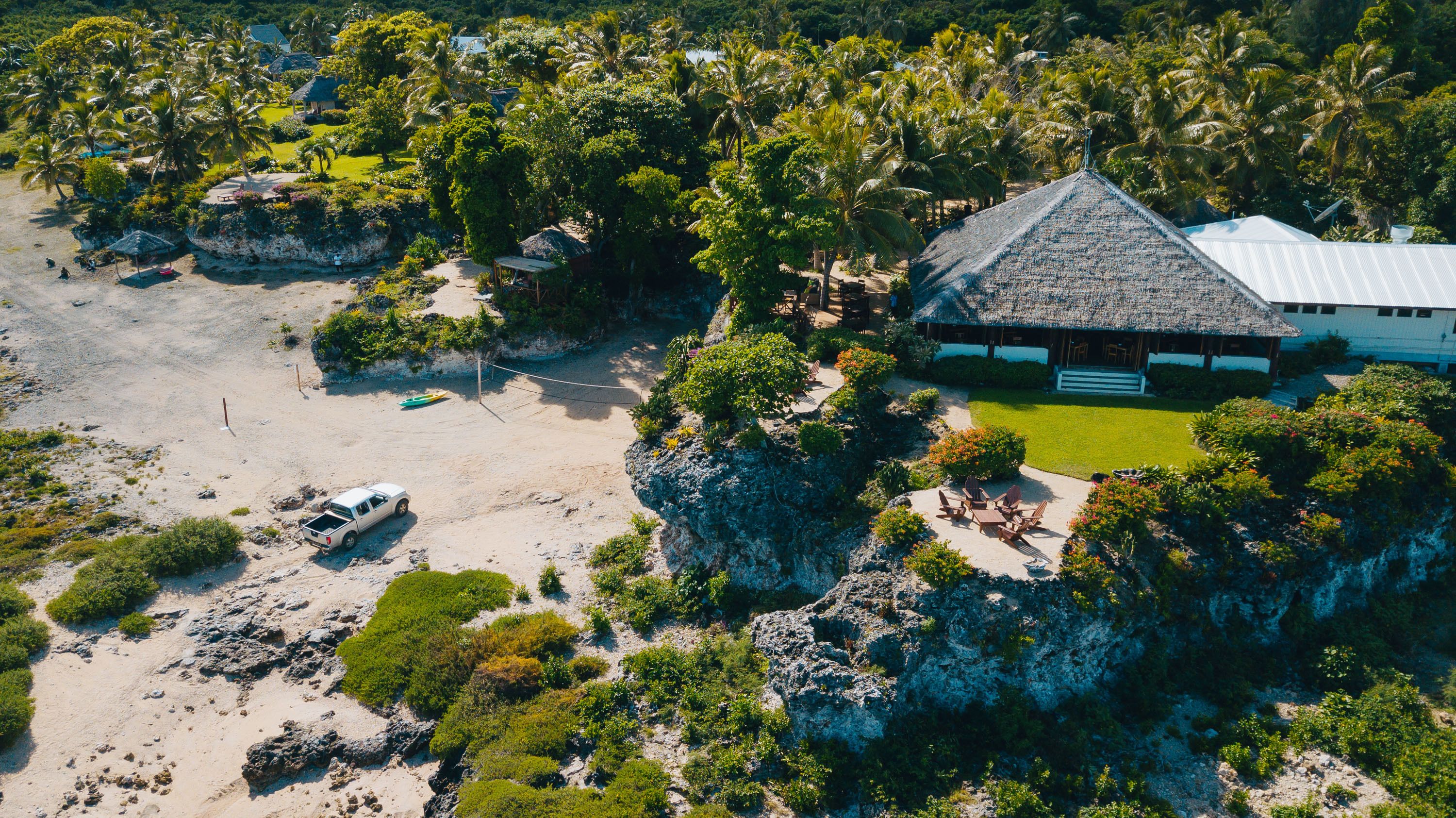 Vista aérea de un resort con una construcción de techo de paja, una playa de arena y vegetación exuberante.
