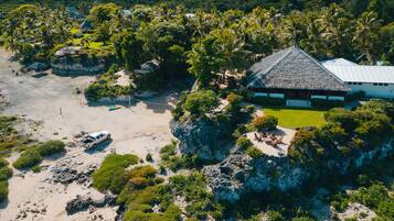 Vista aérea de un resort con una construcción de techo de paja, una playa de arena y vegetación exuberante.
