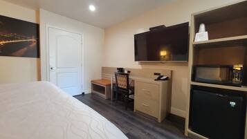 Een hotelkamer met een bed, een bureau met stoel, een televisie, een magnetron en een deur.