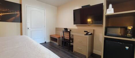 Habitación de hotel con una cama, un escritorio con silla, televisión, microondas y una puerta.