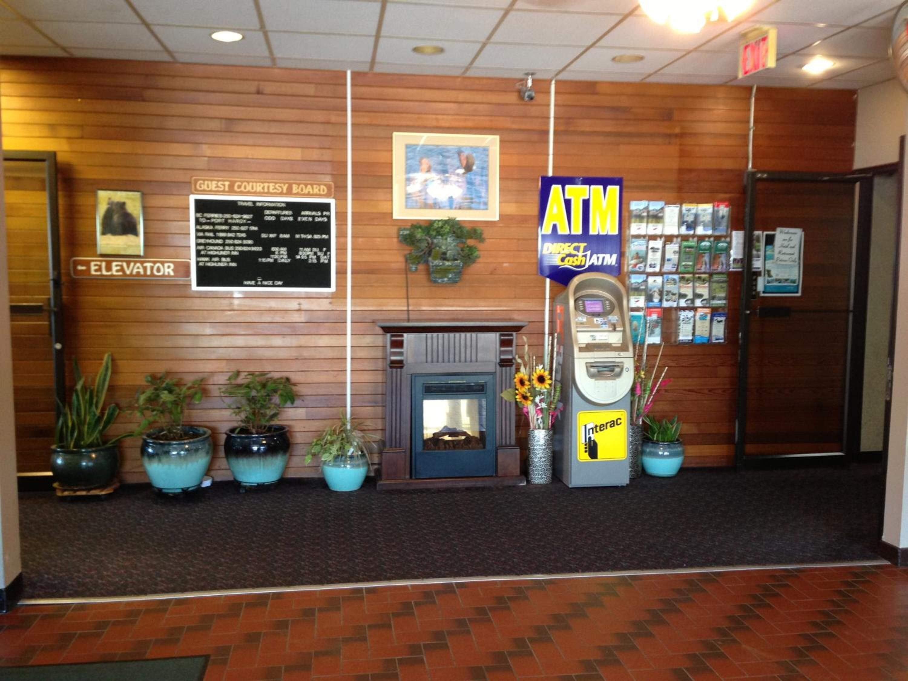 Un hall d’entrée avec un panneau d’affichage pour les visiteurs, un distributeur automatique de billets et des plantes en pot.