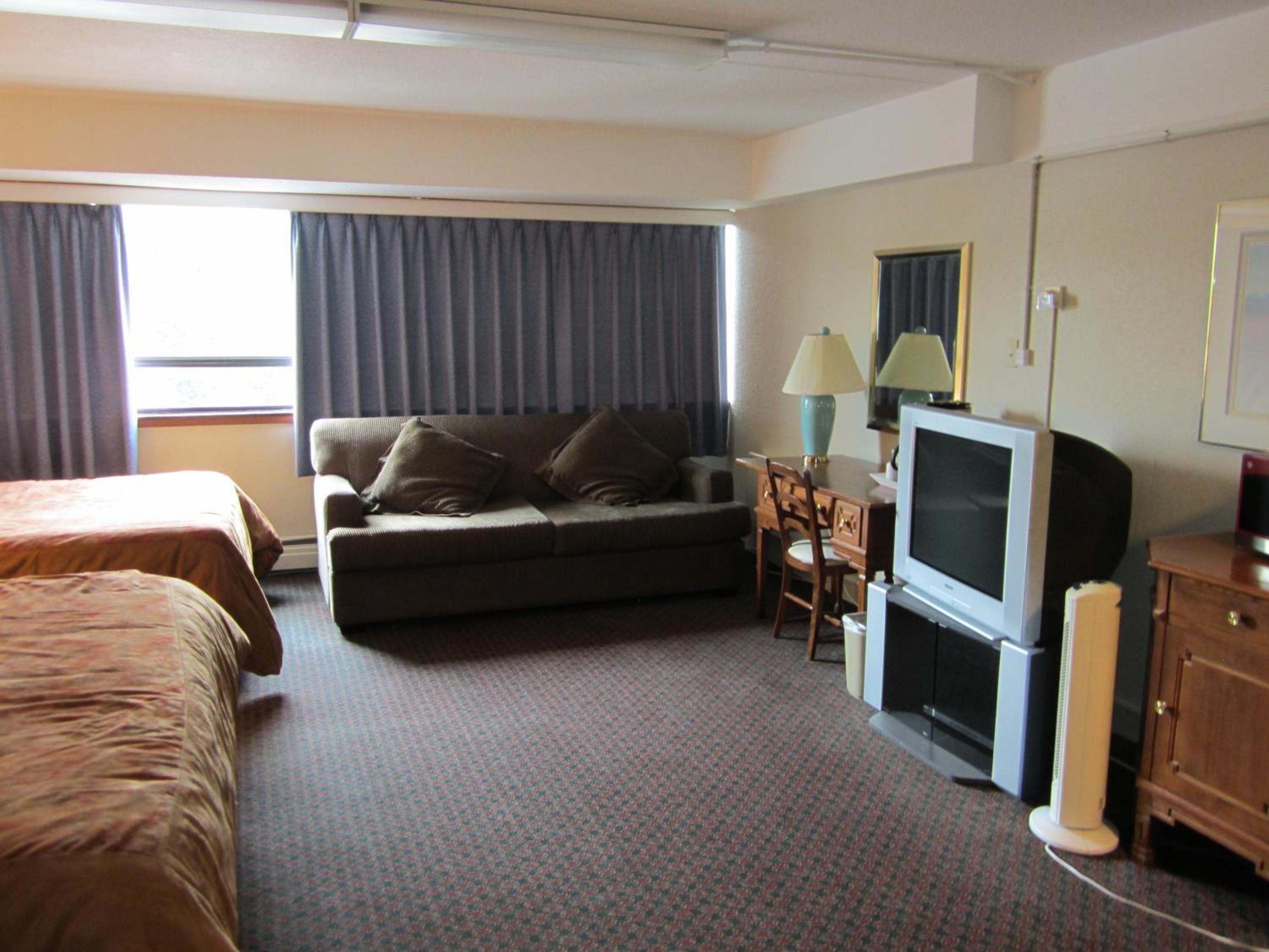 A hotel room with a bed, a sofa, a TV, a desk, and a lamp.