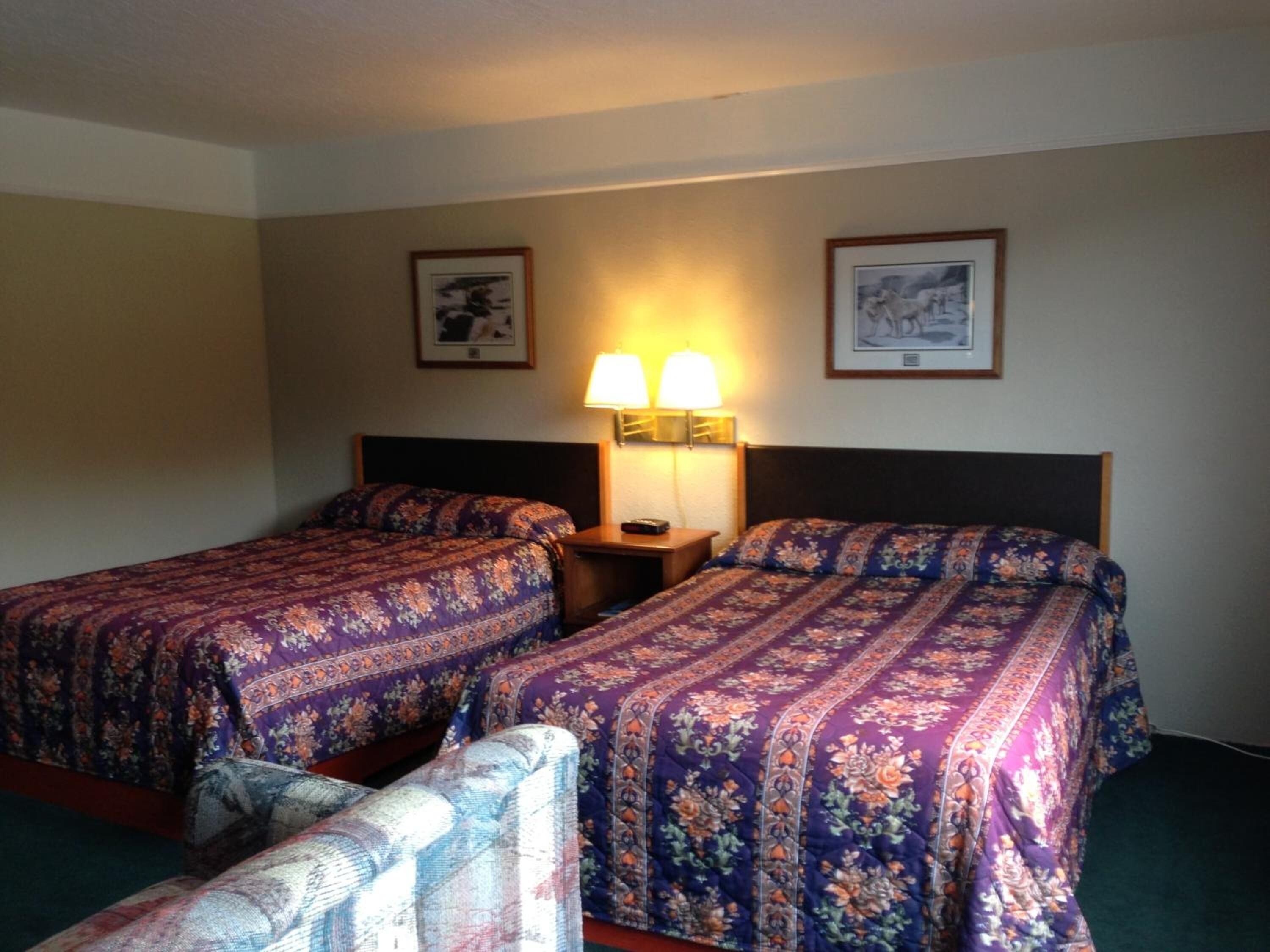 A hotel room with two beds, a nightstand, two wall-mounted lamps, and a chair.