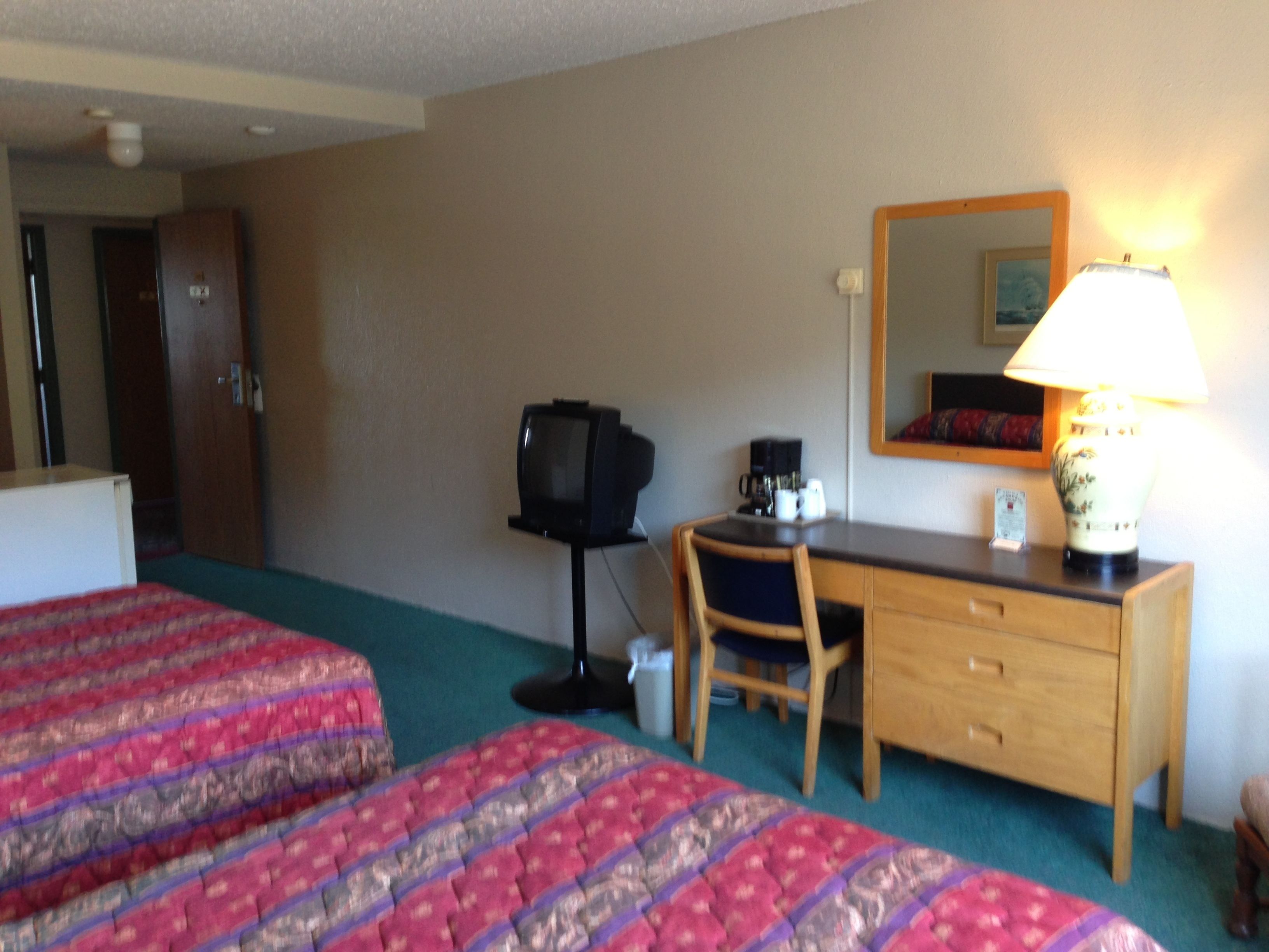 A hotel room with two beds, a desk, a chair, a television, a coffee maker, and a lamp.