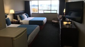 Una habitació d'hotel amb dos llits, televisió, escriptori i finestra amb vista a l'exterior.