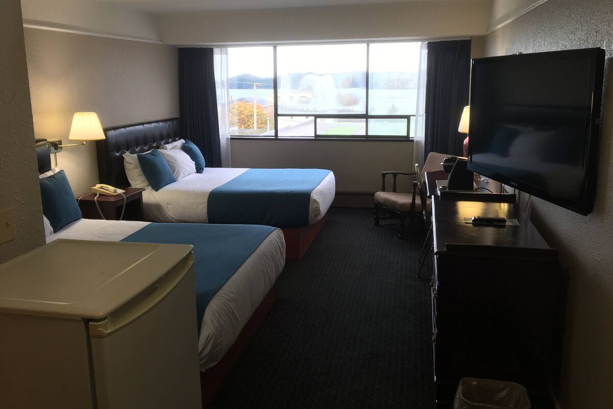 A hotel room with two beds, a TV, a desk, and a window with a view of the outside.