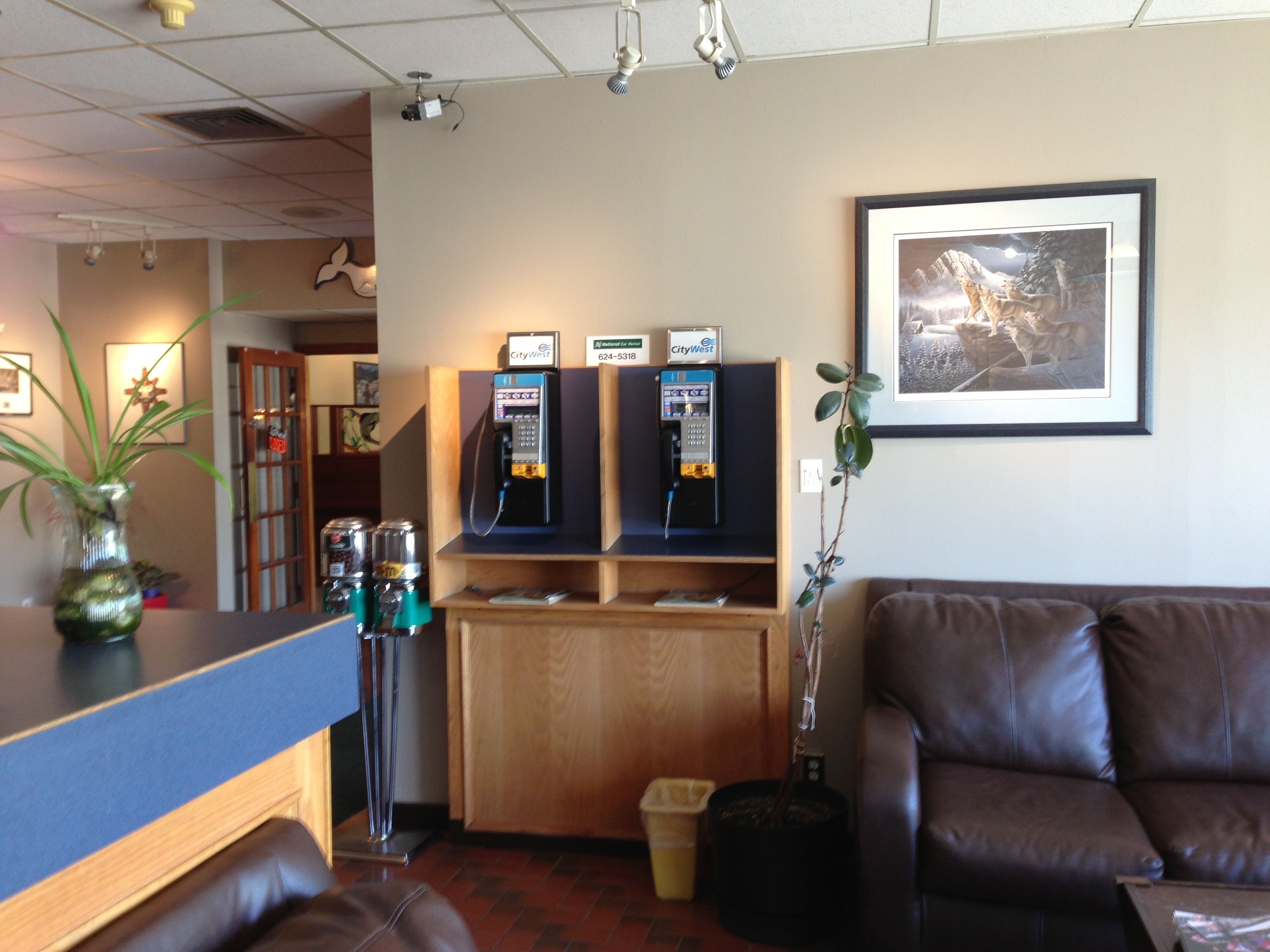 A lobby with a reception desk, two ATMs, a framed picture on the wall, and a brown leather couch.