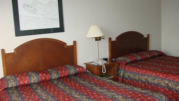 A hotel room with two wooden beds, a bedside table with a lamp, and a framed drawing on the wall.
