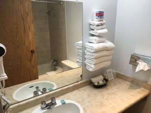 A bathroom with a sink, mirror, and stacked towels.