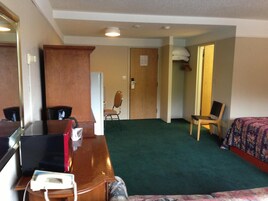 Una habitación de hotel con un escritorio de madera, un teléfono, una silla, una cama con cubrecama floral y una alfombra verde.