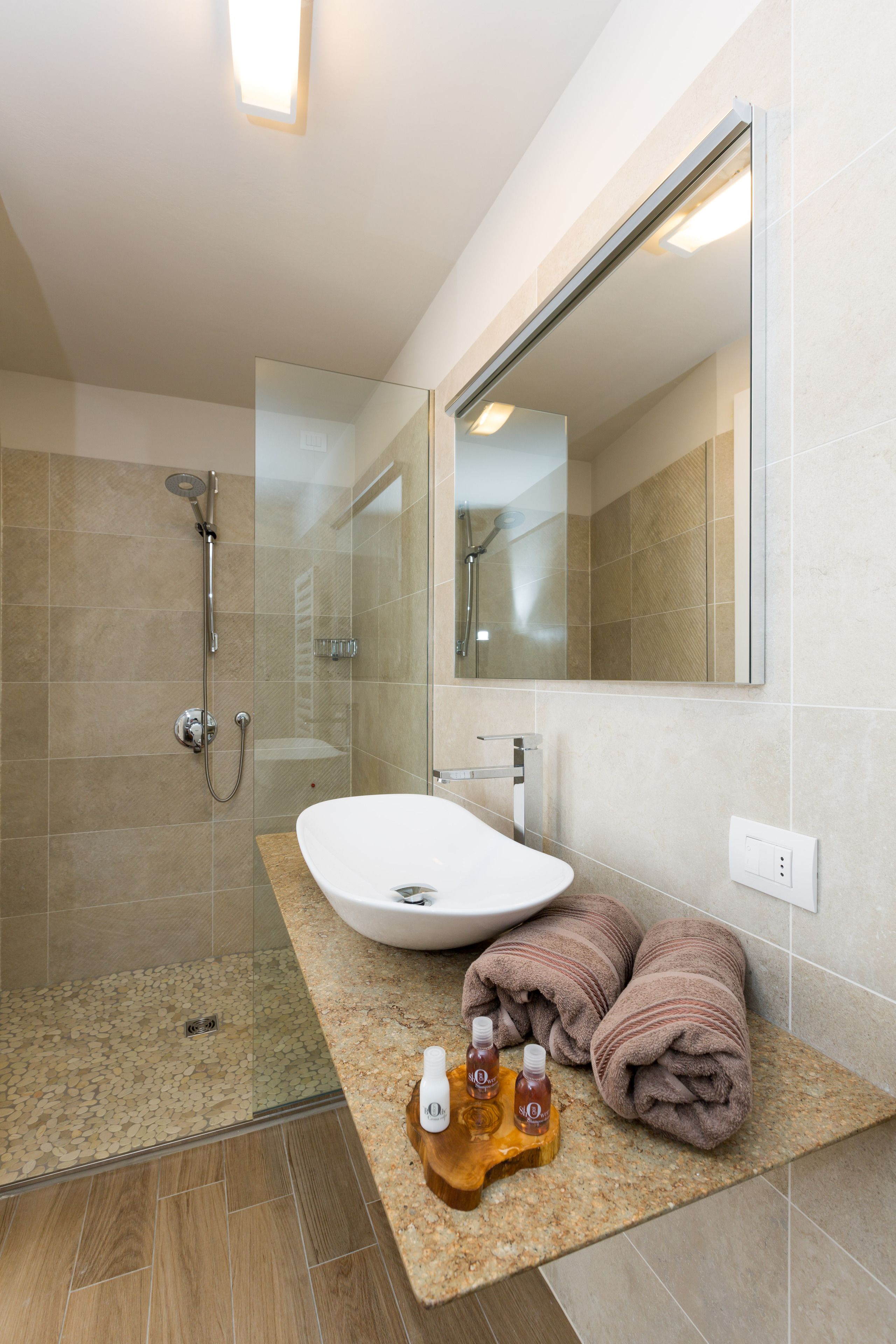 Ein modernes Badezimmer mit einer Glaskabinentrennung, einem weißen Waschbecken und einem großen Spiegel.