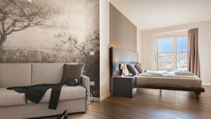 A modern hotel room with a large window, a bed, a sofa, and a wall with a tree mural. - PACE 1954 Hotel (Arco)