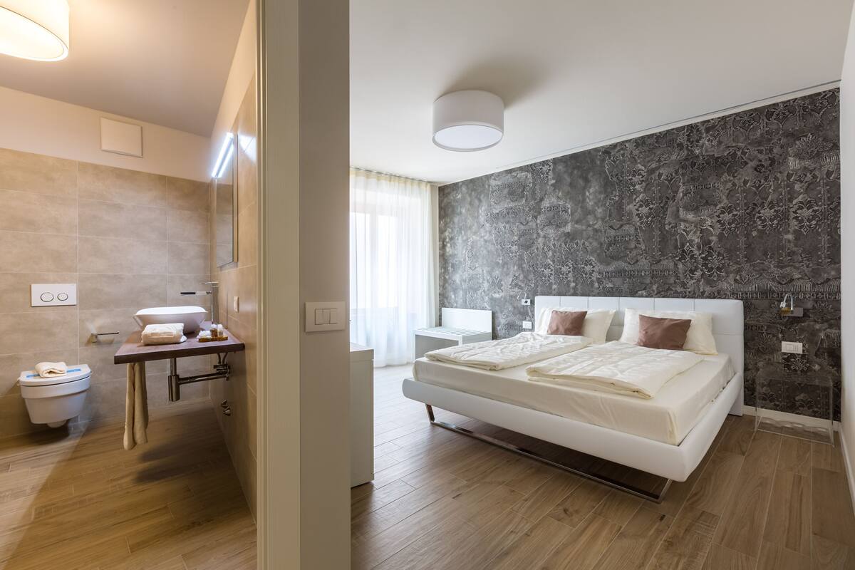A modern bedroom with a large bed, a bedside table, a nightstand, and a dark patterned wall.