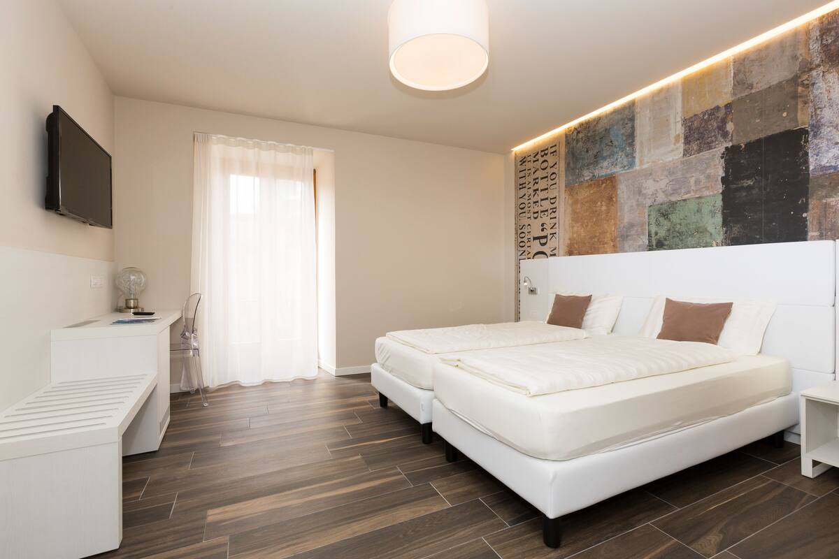 A modern bedroom with a large bed, a desk, and a TV mounted on the wall.