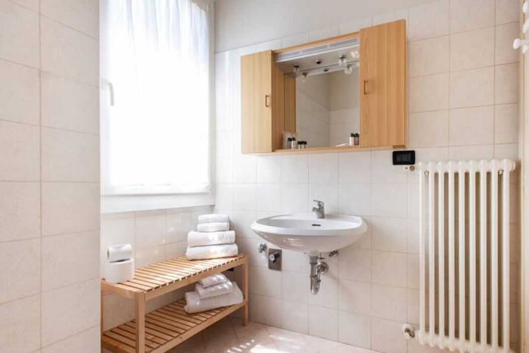 A modern bathroom with a wooden vanity, white tiles, a white sink, and a radiator.