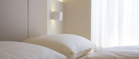 A hotel room with a large bed, a headboard with a light fixture, and a window with sheer curtains.