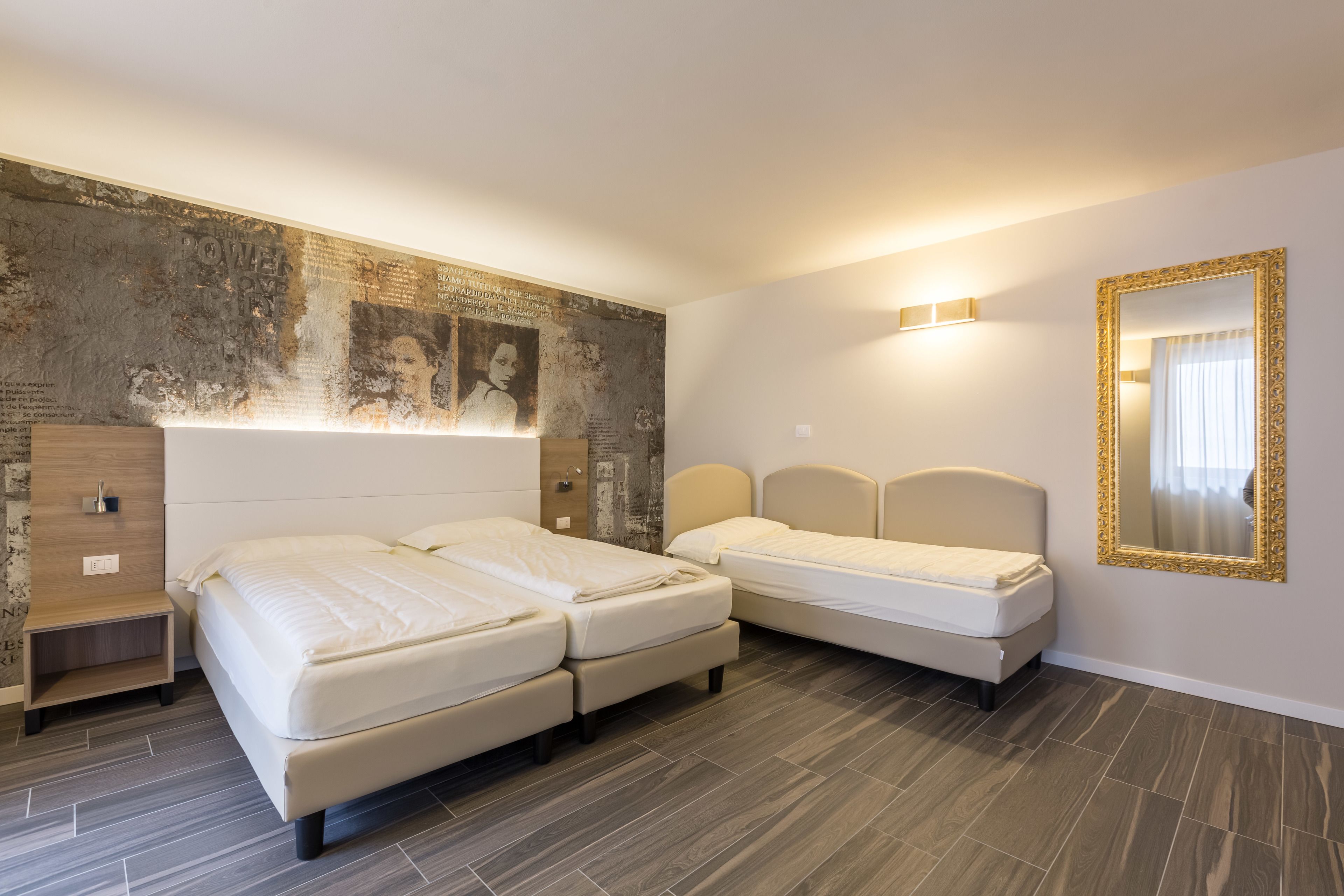 Ein Hotelzimmer mit zwei Betten, einer großen Wandmalerei, einem Spiegel und einem Nachttisch aus Holz.