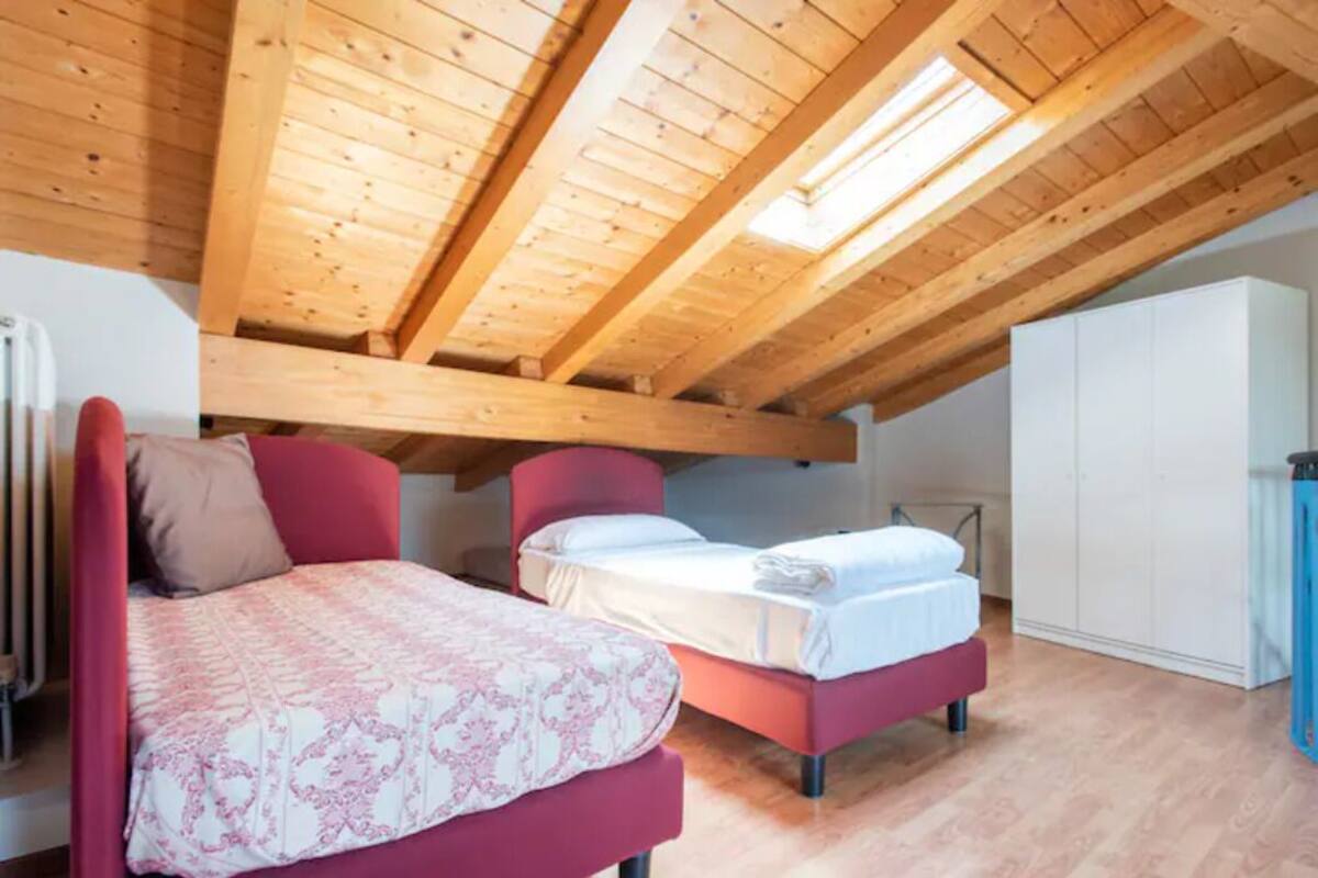 A bedroom with a sloped ceiling, wooden beams, a bed, a chair, and a wardrobe.