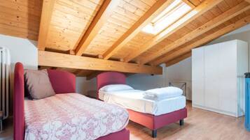 A bedroom with a sloped ceiling, wooden beams, a bed, a chair, and a wardrobe.