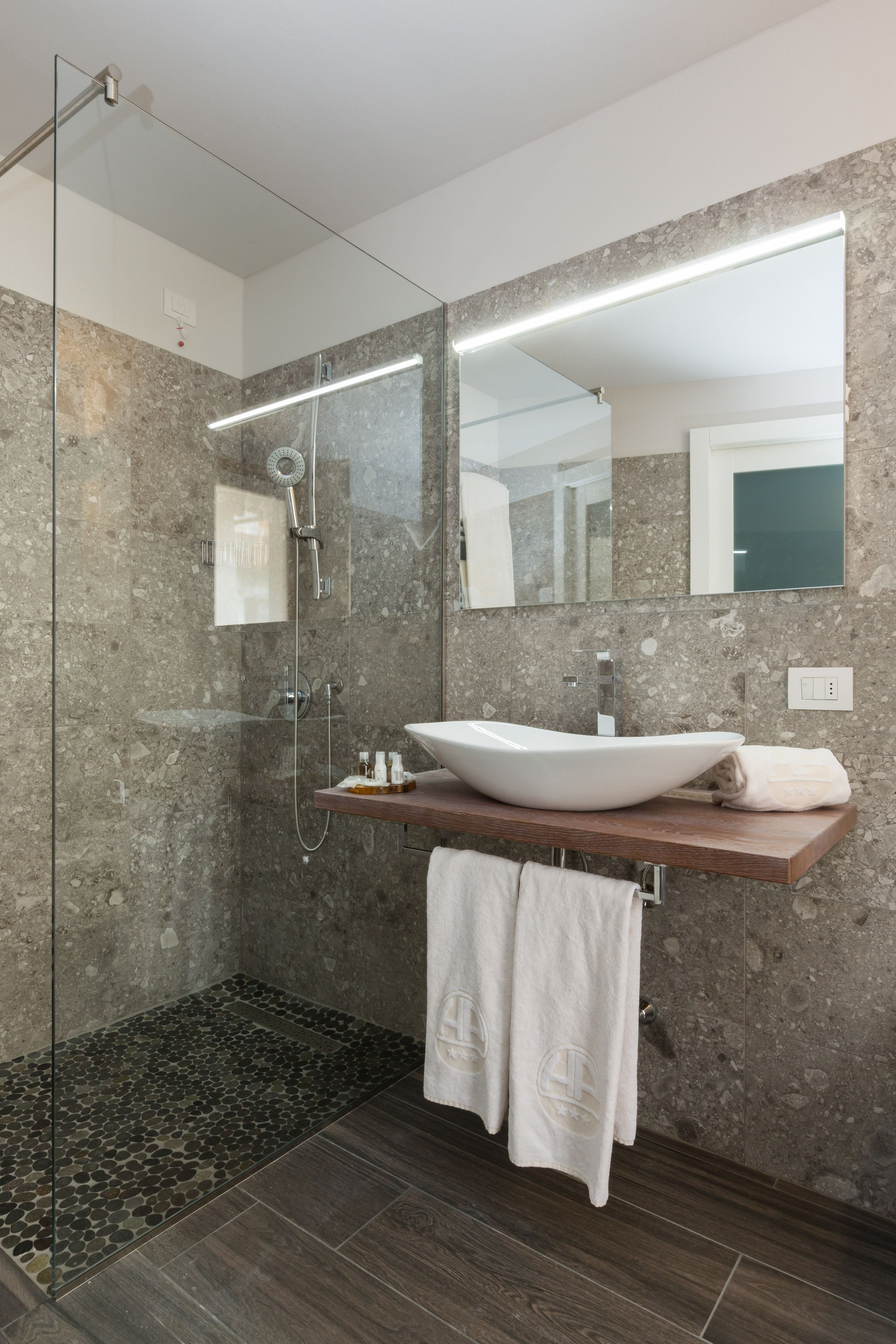 A modern bathroom with a glass-enclosed shower, a large mirror, and a wooden vanity with a vessel sink.