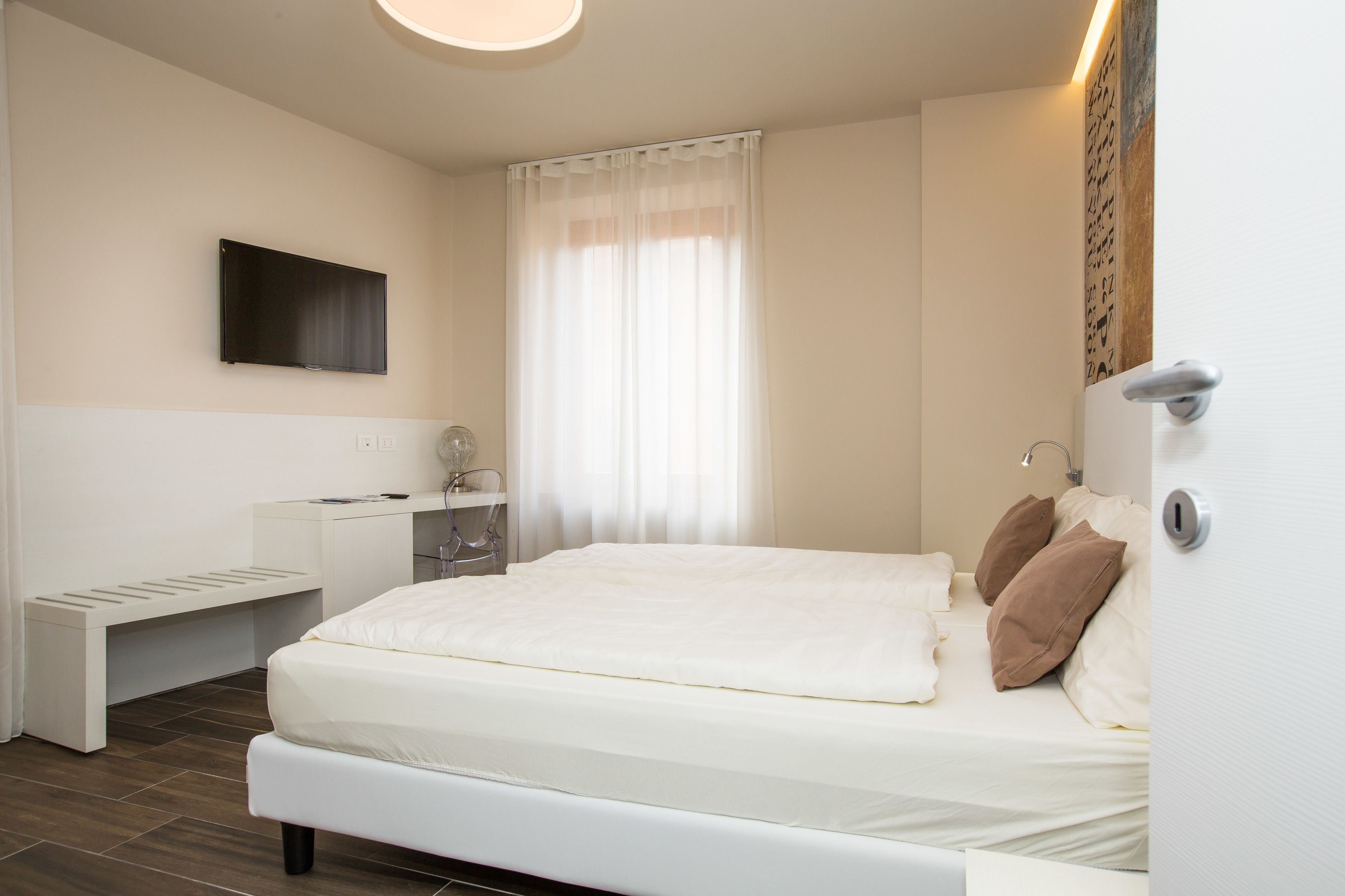 Un dormitorio moderno con una cama grande, una mesita de noche, un espejo y un televisor de pantalla plana montado en la pared.