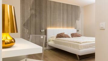 Camera da letto moderna con un letto bianco, un comodino pulito e un pannello imbottito a effetto strisce.