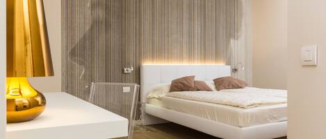 A modern bedroom with a white bed, a clear bedside table, and a striped wallpaper headboard.