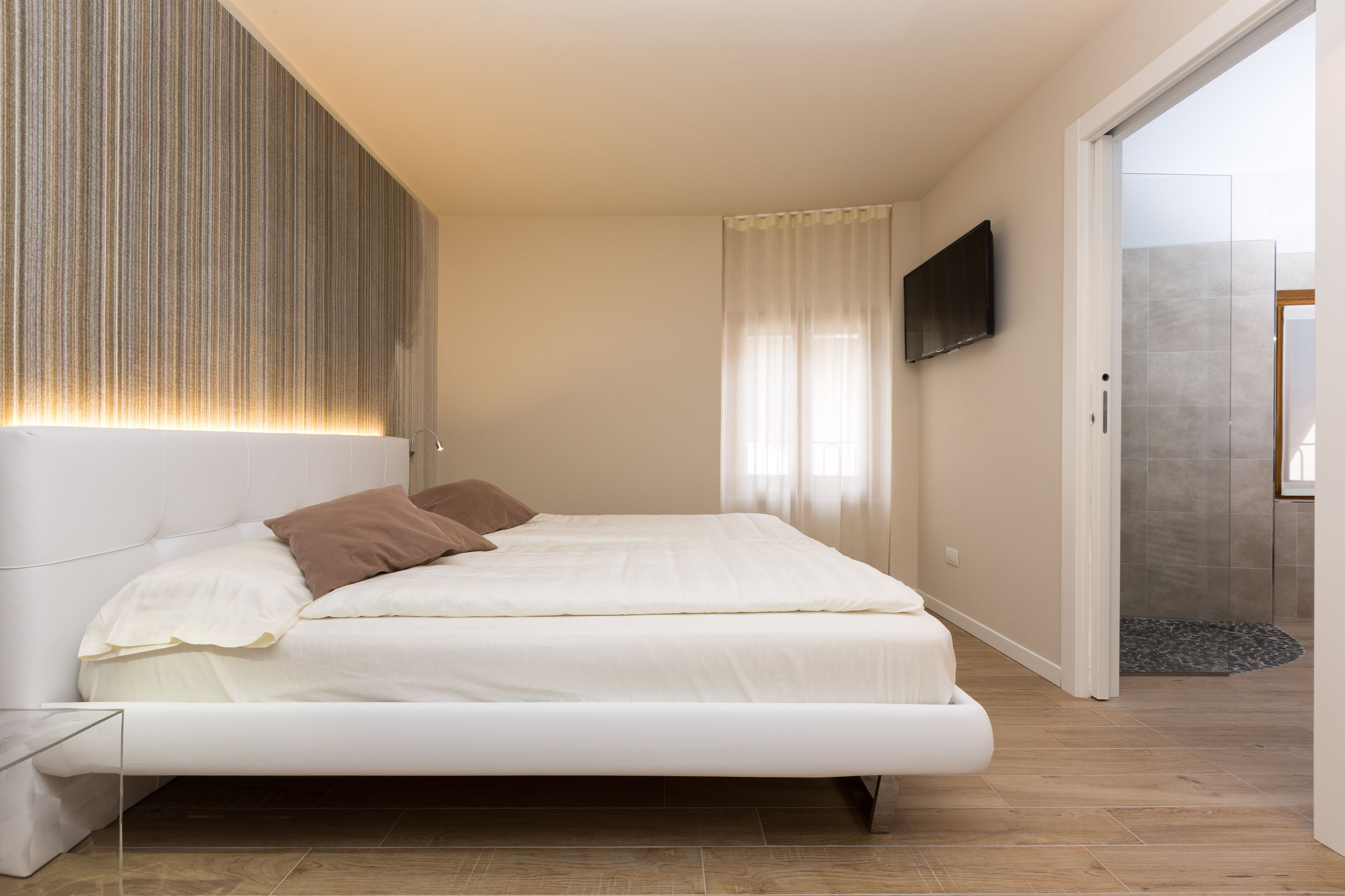 Une chambre moderne avec un grand lit, un téléviseur à écran plat fixé au mur et une porte-fenêtre coulissante donnant sur une salle de bain.