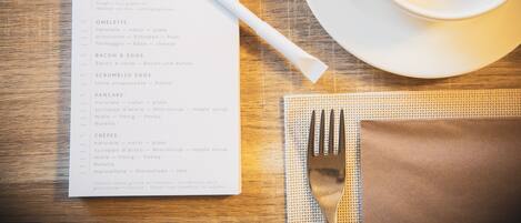 A breakfast menu on a wooden table with a cup of coffee and a fork.
