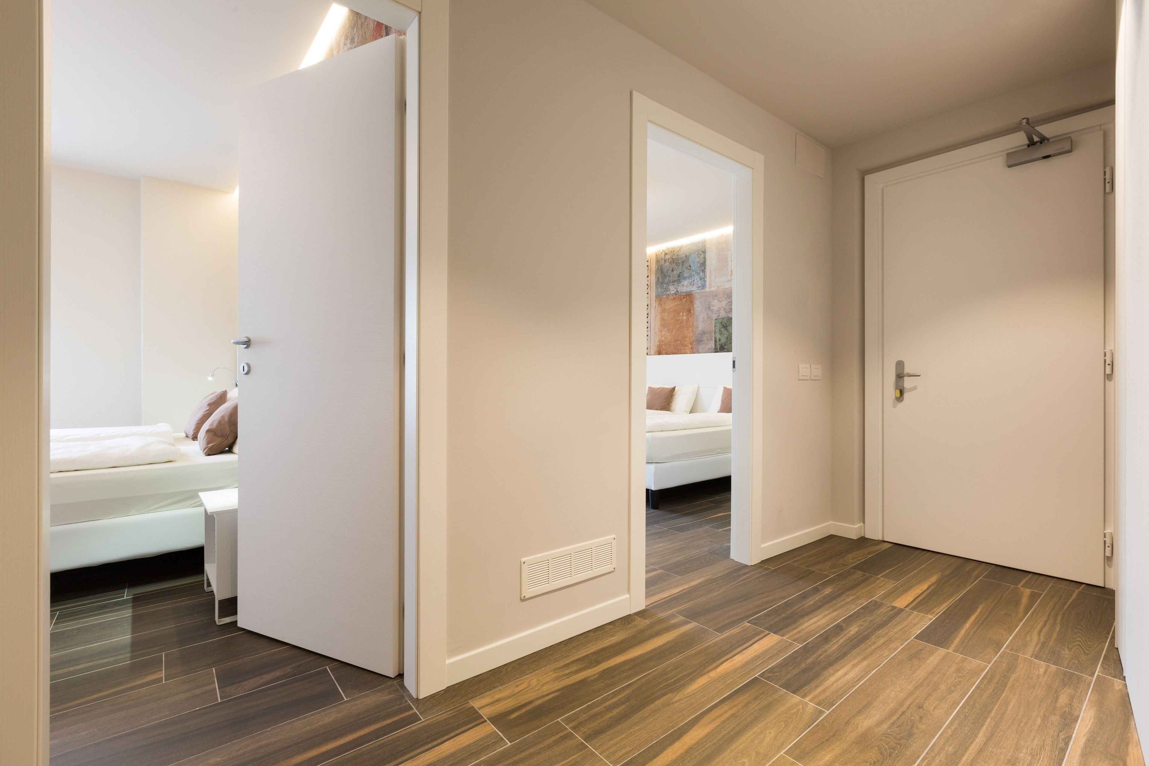 A modern hotel room with a bed, bedside table, and a door leading to another room.